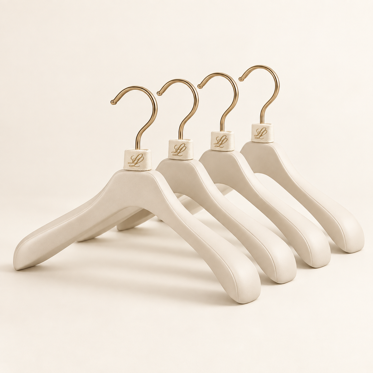 Set of four warm-ivory structured wardrobe hangers with champagne-gold hooks and woven LL monogram loops.