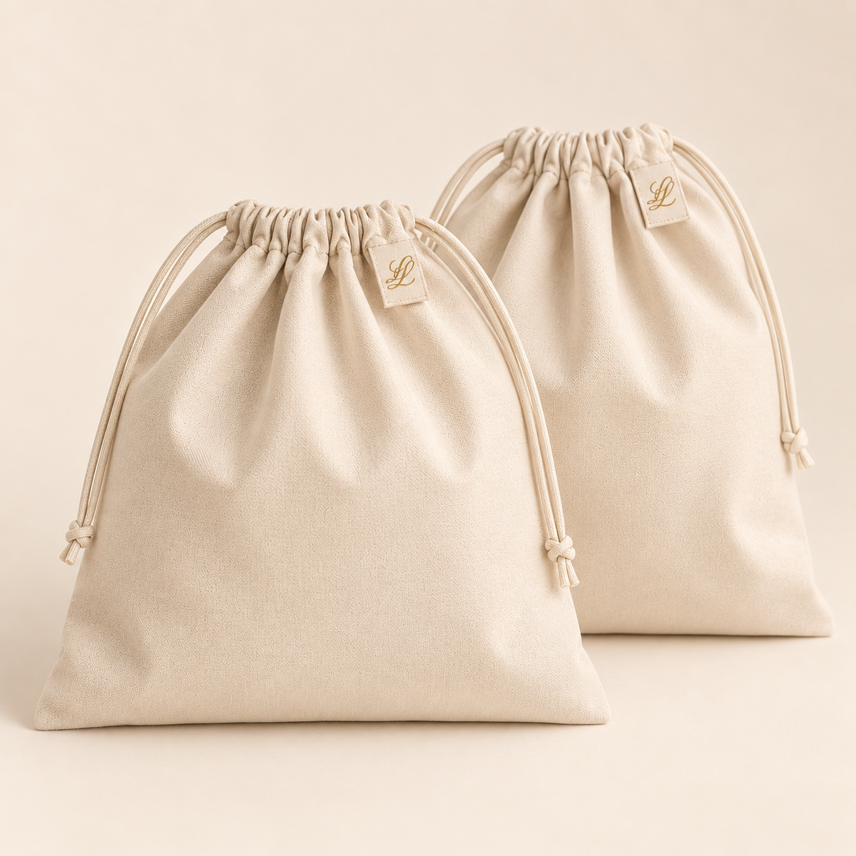 Pair of warm-ivory wardrobe dust bags with matching drawstrings and discreet champagne-gold LL woven tabs.